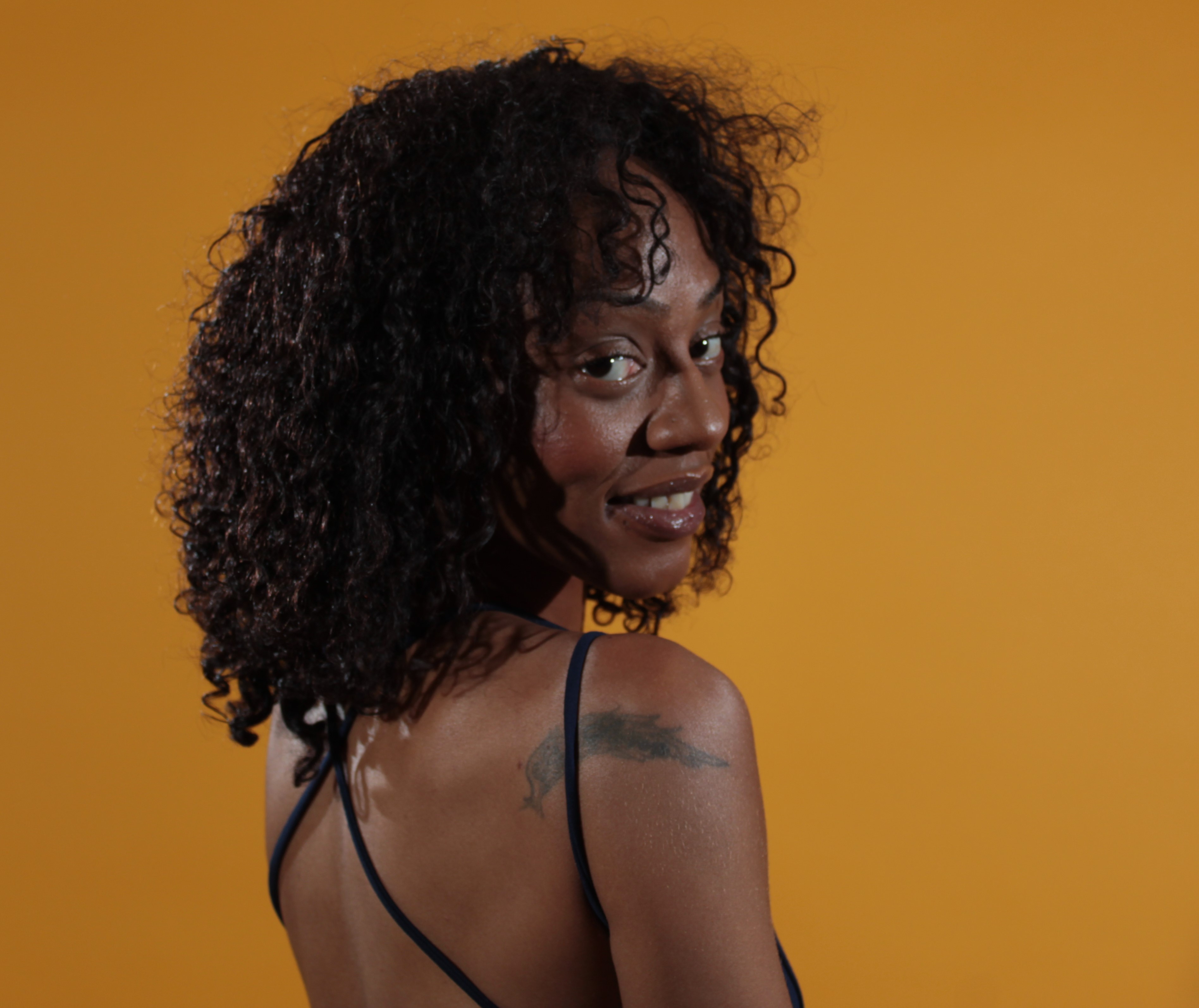 Headshot of black female looking back at us over her shoulder. Yellow Background.