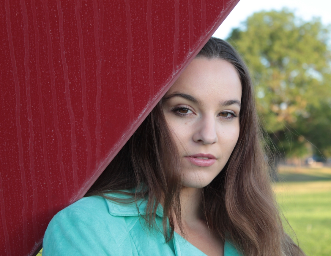 head shot of female by red metal sculpture in the park