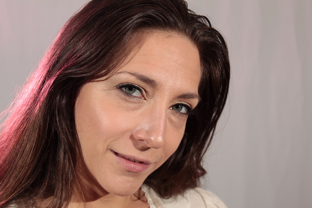brunette female headshot against white backdrop with a hint of pink gel light on the side