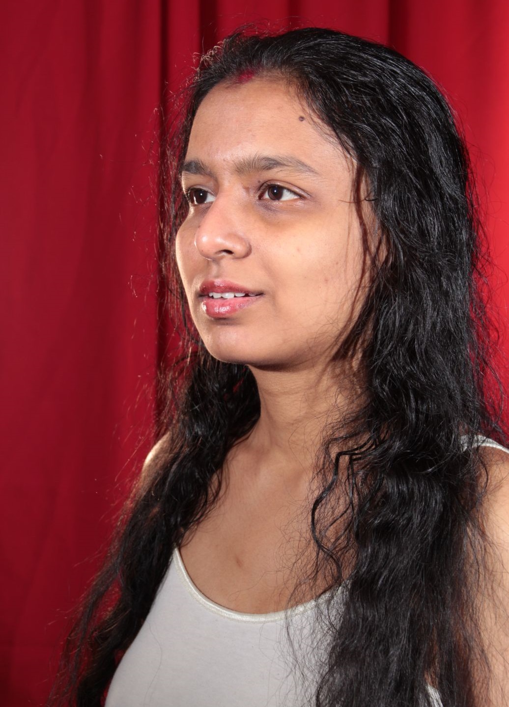 India woman in white top against red curtain